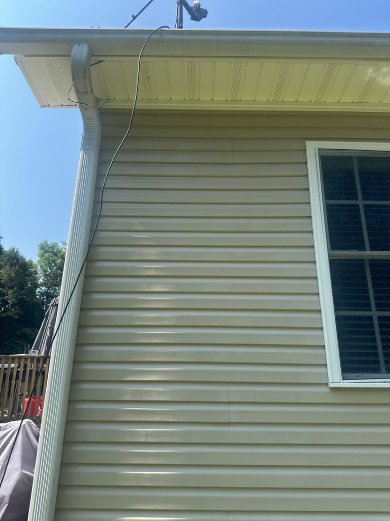 cable running from a roof to a house for power washing service on light vinyl siding